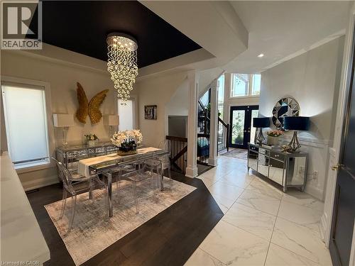 Dining space featuring a tray ceiling, a chandelier, marble look tile flooring, and stairs - 11 Donatello Court, Hamilton, ON - Indoor