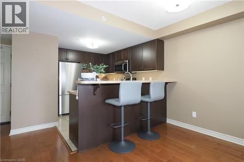 Kitchen with dark brown cabinetry, a kitchen breakfast bar, stainless steel appliances, light countertops, and a peninsula - 645 St. David Street S Unit# 412, Fergus, ON - Indoor Photo Showing Kitchen