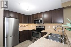 Kitchen with newly upgraded stainless steel fridge, stainless steel stove and OTR rangehood/microwave, dark brown cabinets, light countertops, and light tile flooring. - 