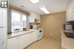 Common room kitchen featuring white cabinetry, white appliances, light countertops, under cabinet range hood, and light tile flooring - 