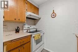 Kitchen featuring white range with electric stovetop, under cabinet range hood, light countertops, backsplash, and brown cabinetry - 