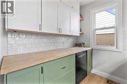 Kitchen featuring wood counters, green cabinetry, open shelves, dishwasher, and decorative backsplash - 