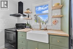 Kitchen featuring green cabinetry, black electric range, wall chimney exhaust hood, open shelves, and crown molding - 