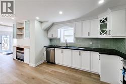 Kitchen featuring glass insert cabinets, backsplash, white cabinetry, light wood-style flooring, and stainless steel dishwasher - 
