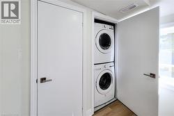 Laundry room with stacked washing machine and dryer, wood finished floors, and lofted ceiling - 