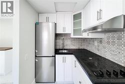 Kitchen featuring freestanding refrigerator, decorative backsplash, black electric cooktop, white cabinets, and under cabinet range hood - 