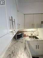 Kitchen featuring white cabinets, decorative backsplash, stainless steel microwave, and light stone countertops - 