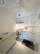 Kitchen featuring white appliances, tasteful backsplash, white cabinets, under cabinet range hood, and a ceiling fan - 