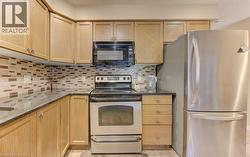 Kitchen featuring appliances with stainless steel finishes, decorative backsplash, dark stone countertops, and light brown cabinetry - 