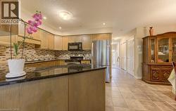 Kitchen with a peninsula, dark stone counters, appliances with stainless steel finishes, decorative backsplash, and light tile patterned flooring - 