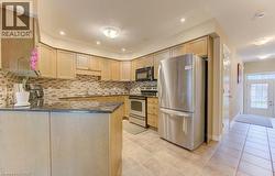 Kitchen featuring appliances with stainless steel finishes, light brown cabinets, dark stone countertops, a peninsula, and backsplash - 