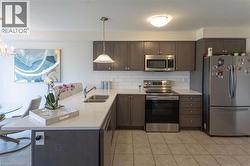 Kitchen featuring appliances with stainless steel finishes, decorative backsplash, light tile patterned flooring, and dark brown cabinets - 
