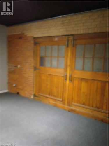 Empty room with brick wall, carpet floors, and wooden walls - 12 Ferguson Avenue N, Hamilton, ON 
