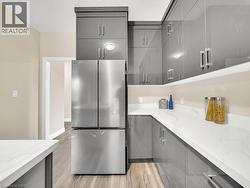 Kitchen with gray cabinets, freestanding refrigerator, light wood-type flooring, and light stone counters - 