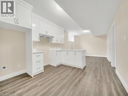 Kitchen featuring a peninsula, white cabinets, light wood-style flooring, light countertops, and under cabinet range hood - 