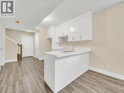 Kitchen featuring light countertops, white cabinetry, light wood-type flooring, a peninsula, and under cabinet range hood - 