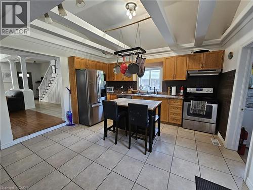 Kitchen with light tile patterned floors, appliances with stainless steel finishes, brown cabinets, beam ceiling, and tasteful backsplash - 253 Mary Street, Hamilton, ON - Indoor Photo Showing Kitchen