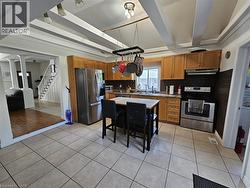 Kitchen with light tile patterned floors, appliances with stainless steel finishes, brown cabinets, beam ceiling, and tasteful backsplash - 