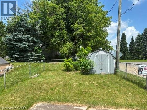 Fenced yard featuring a gray storage shed and mature trees - 13 Second Avenue E, Simcoe, ON 