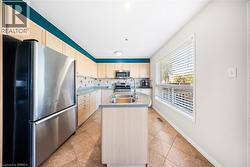 Kitchen with stainless steel appliances, backsplash, light tile patterned floors, a center island with sink, and light brown cabinets - 