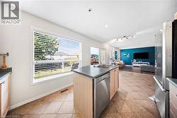 Kitchen featuring dark countertops, an island with sink, appliances with stainless steel finishes, light brown cabinetry, and light tile patterned floors - 