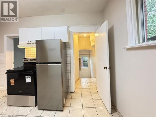 Kitchen with stainless steel appliances, under cabinet range hood, light tile patterned floors, and white cabinetry - 24 Somerset Avenue, Hamilton, ON - Indoor Photo Showing Kitchen