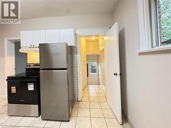 Kitchen with stainless steel appliances, under cabinet range hood, light tile patterned floors, and white cabinetry - 