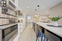 Kitchen featuring appliances with stainless steel finishes, white cabinets, decorative light fixtures, light stone counters, and recessed lighting - 