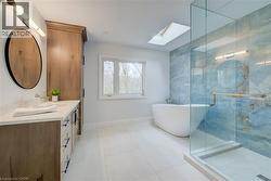 Full bathroom featuring a skylight, a soaking tub, double vanity, a stall shower, and light tile patterned floors - 
