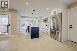 Kitchen featuring freestanding refrigerator, white cabinets, an island with sink, hanging light fixtures, and tasteful backsplash - 