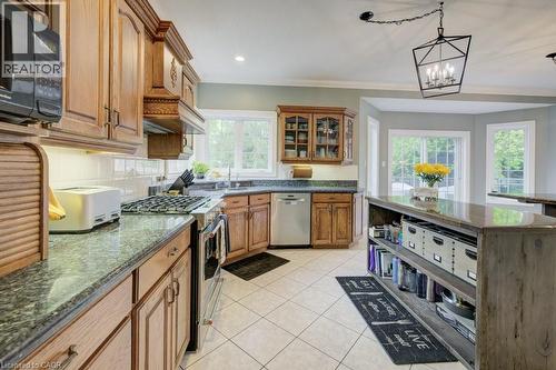 Kitchen with appliances with stainless steel finishes, brown cabinetry, tasteful backsplash, light tile patterned floors, and dark stone countertops - 1525 Dickie Settlement Road, Cambridge, ON - Indoor Photo Showing Kitchen With Double Sink