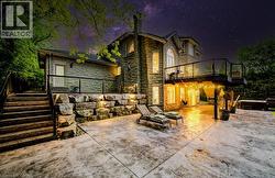 Back of house at twilight featuring a patio, stone siding, a chimney, and stairway - 