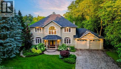 View of front of house with stone siding, an attached garage, decorative driveway, a chimney, and a lawn - 1525 Dickie Settlement Road, Cambridge, ON - Outdoor