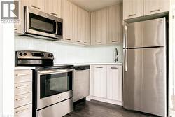 Kitchen featuring appliances with stainless steel finishes, light countertops, backsplash, dark wood finished floors, and light brown cabinets - 