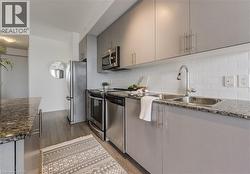 Kitchen featuring light wood-type flooring, decorative backsplash, gray cabinets, appliances with stainless steel finishes, and a sink - 