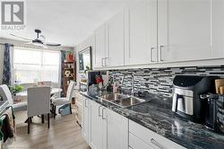 Kitchen featuring a sink, tasteful backsplash, a ceiling fan, white cabinets, and light wood-type flooring - 