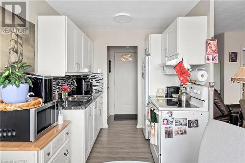 Kitchen featuring white appliances, light wood-style flooring, white cabinets, decorative backsplash, and baseboards - 485 Thorold Road Unit# 323, Welland, ON - Indoor Photo Showing Kitchen With Double Sink