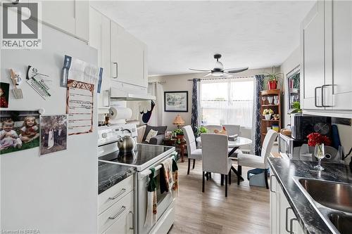 Kitchen featuring white appliances, under cabinet range hood, dark countertops, light wood-type flooring, and white cabinets - 485 Thorold Road Unit# 323, Welland, ON - Indoor Photo Showing Other Room