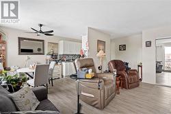 Living room with a ceiling fan, light wood-style flooring, and baseboards - 