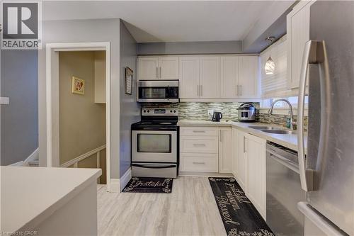 Kitchen with stainless steel appliances, decorative backsplash, light stone counters, light wood-style floors, and hanging light fixtures - 31 Bonfair Court, Kitchener, ON - Indoor Photo Showing Kitchen With Double Sink
