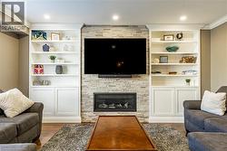 Living area with wood finished floors, a stone fireplace, crown molding, recessed lighting, and built in features - 