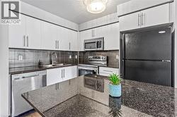 Kitchen featuring appliances with stainless steel finishes, white cabinets, tasteful backsplash, and dark stone countertops - 