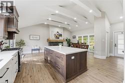 Kitchen with dark brown cabinets, stainless steel range with gas stovetop, light wood-type flooring, beam ceiling, and a center island - 