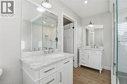 Bathroom featuring a stall shower, two vanities, light wood-type flooring, and recessed lighting - 
