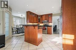 Kitchen featuring stainless steel appliances, light tile patterned floors, a kitchen bar, brown cabinets, and recessed lighting - 