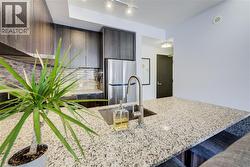 Kitchen featuring freestanding refrigerator, dark brown cabinets, light stone counters, modern cabinets, and track lighting - 