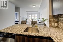 Kitchen featuring dark brown cabinetry, tasteful backsplash, stainless steel dishwasher, light stone counters, and open floor plan - 
