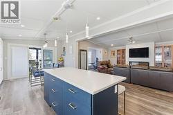 Kitchen with blue cabinetry, hanging light fixtures, a kitchen island, light wood-type flooring, and light countertops - 
