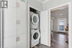 Laundry area featuring crown molding, stacked washer and clothes dryer, and dark wood-type flooring - 