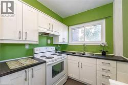 Kitchen with white electric range oven, under cabinet range hood, white cabinetry, dark countertops, and dark tile patterned flooring - 